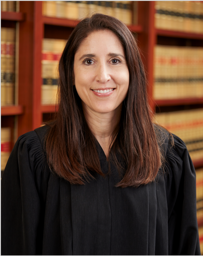 Chief justice patricia guerrero in court robe standing in front of rows of law books